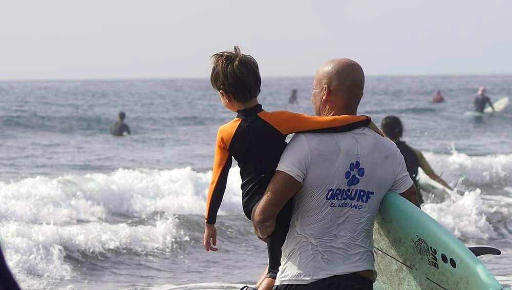 Ori Surf instructor carrying a child towards the waves in El Médano